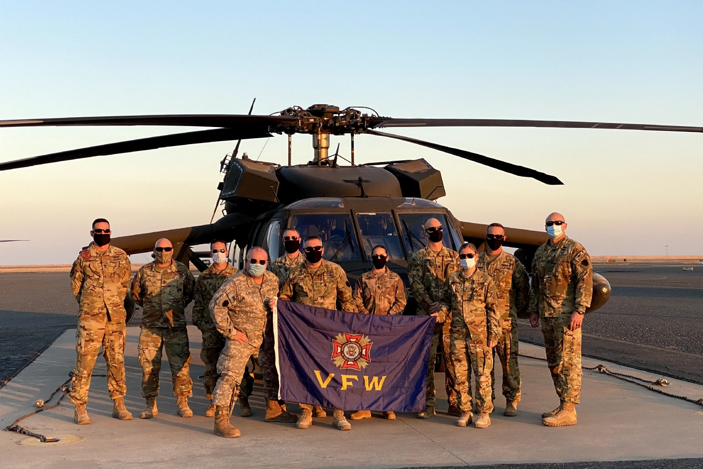 The 28th Infantry Division Expeditionary Combat Aviation Brigade poses with a VFW flag in front of a Blackhawk helicopter. The flag has traveled around the world to units with care packages. It hangs at PA VFW HQs with these photos around it. David Sandman, former Director of Communications, began the tradition.